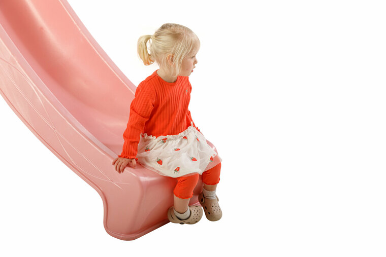 meisje zit op uiteinde pastel roze glijbaan